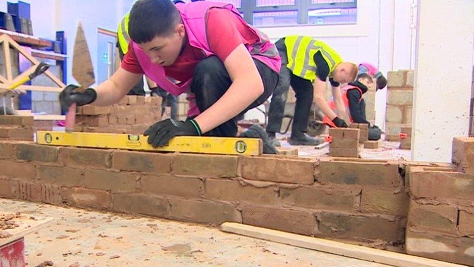 Young man in hi vis vest training how to build a brick wall