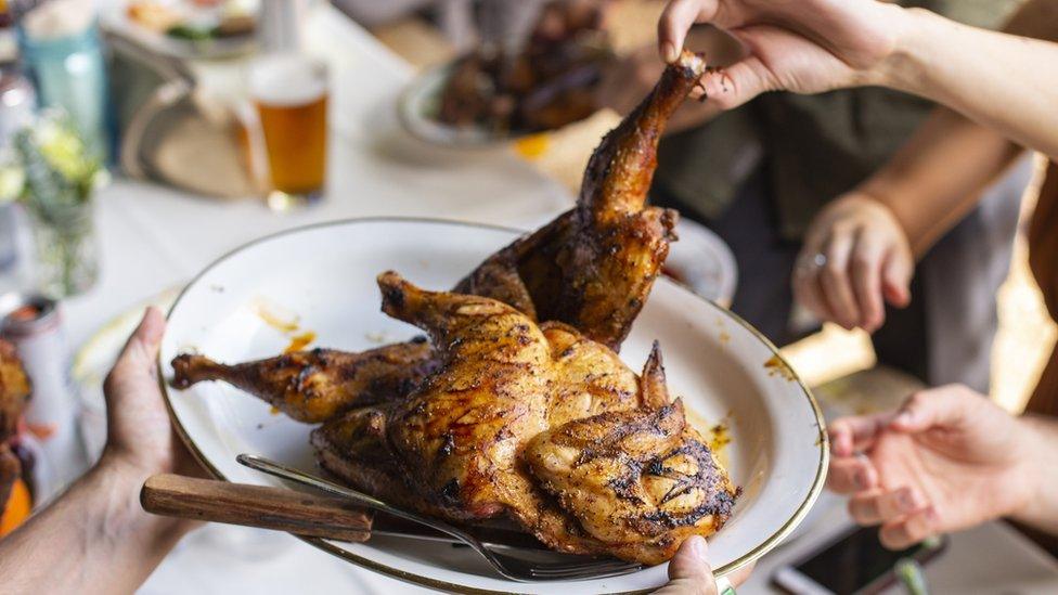 People grabbing chicken off the a serving plate at a family style dinner