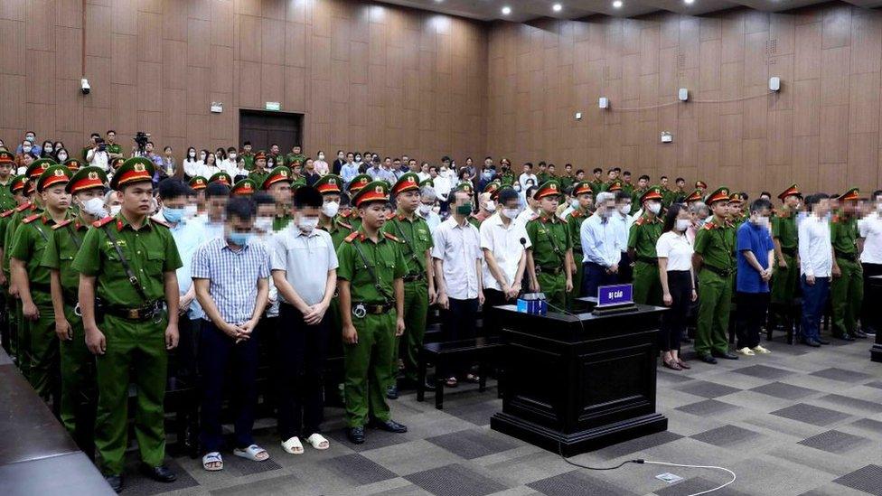 This picture taken and released by the Vietnam News Agency on July 28, 2023 shows defendants (in civil shirts) standing for sentencing in a Hanoi courtroom for the repatriation flight trial.