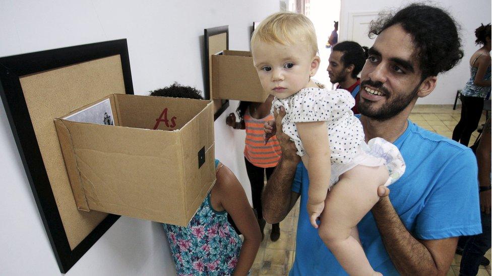 Cuban graffiti artist Danilo Maldonado holds his daughter during a photo exhibition in Havana