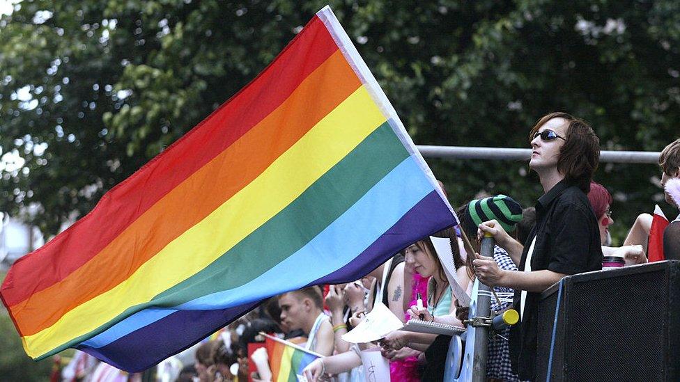 A man waves a rainbow flag on top of a bus