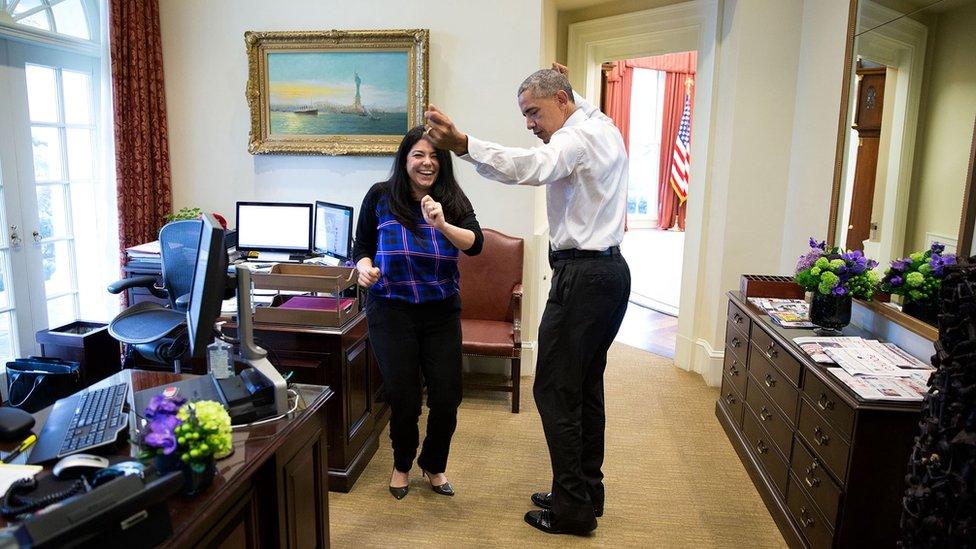 Obama dances, arms outstretched, with a staff member in the reception room adjacent to the oval office. The staff member is laughing looking directly at the camera.