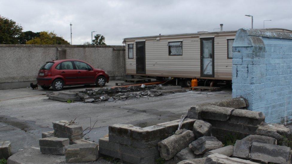 General view of site with caravan, car and rubble.