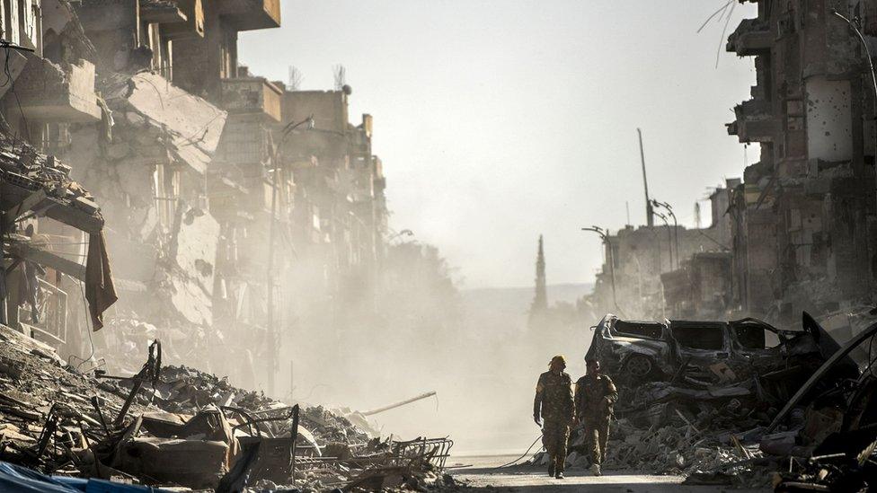 Syrian Democratic Forces (SDF) fighters walk down a devastated street in Raqqa, Syria (20 October 2017)