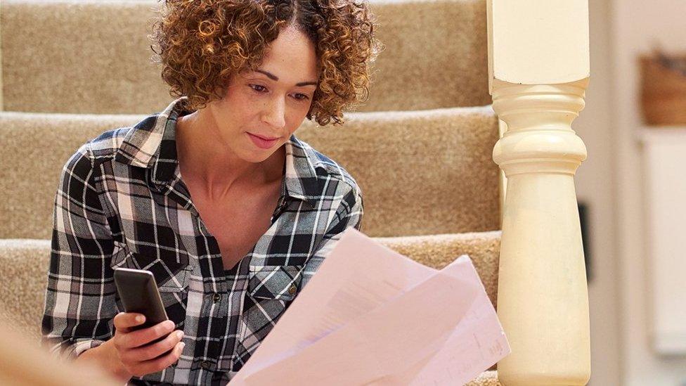 A woman sitting on the stairs holding a phone and some bills