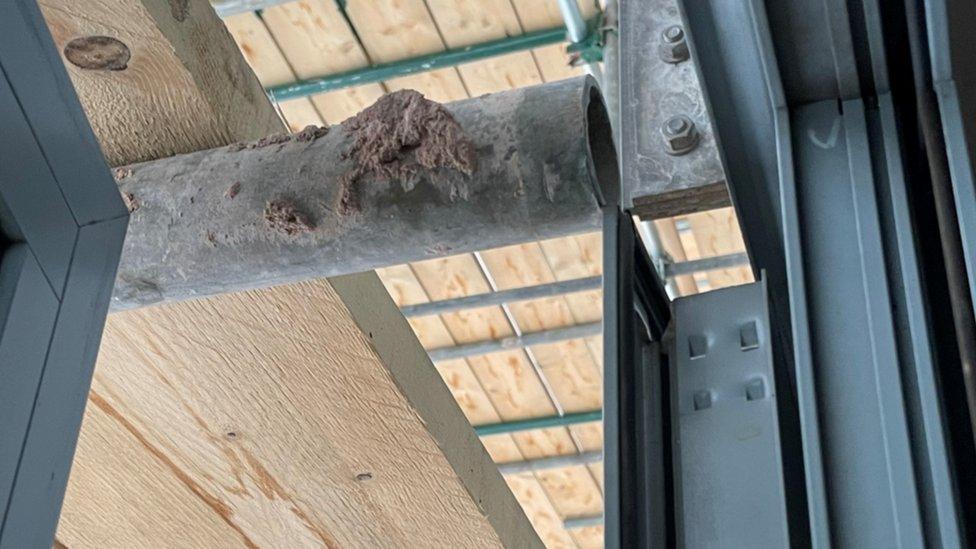 An improperly positioned scaffolding pole prevents a window from opening beyond a fraction of a centimetre at Jim and Katie's flat