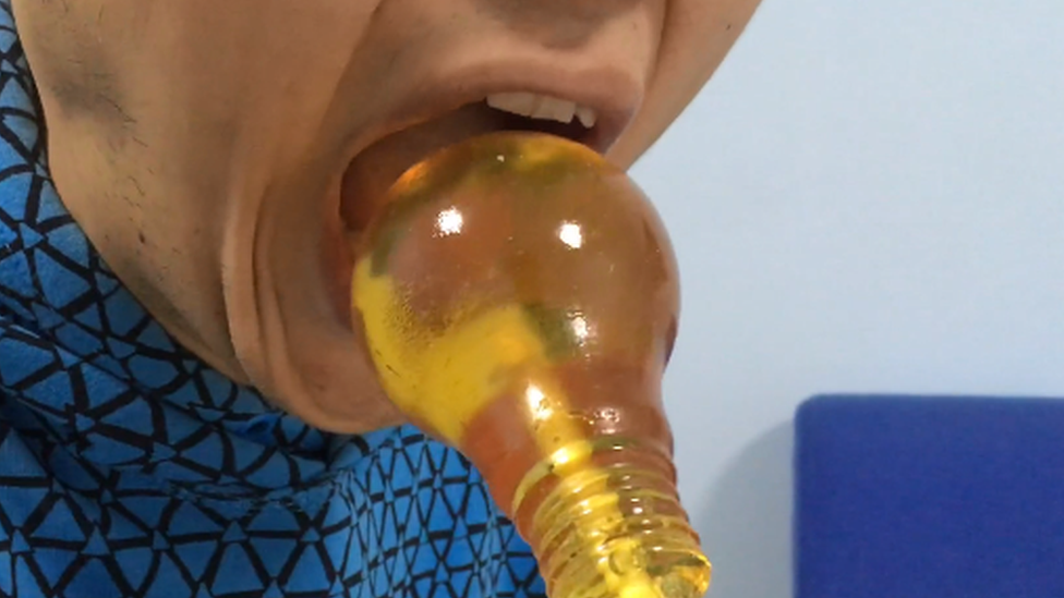 Man trying to fit a light bulb shaped sweet in his mouth