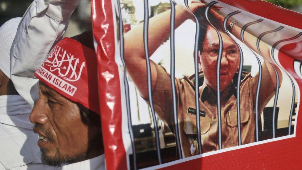 A Muslim protester holds a banner with picture depicting Jakarta Governor Basuki Tjahaja Purnama, popularly known as "Ahok," behind bars during a rally outside the court where his trial hearing of is held in Jakarta, Indonesia, on 20 December 2016