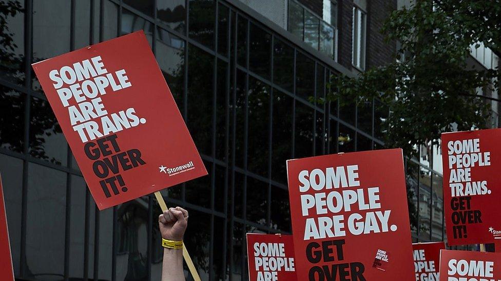 people marching with signs reading 'some people are trans, get over it'