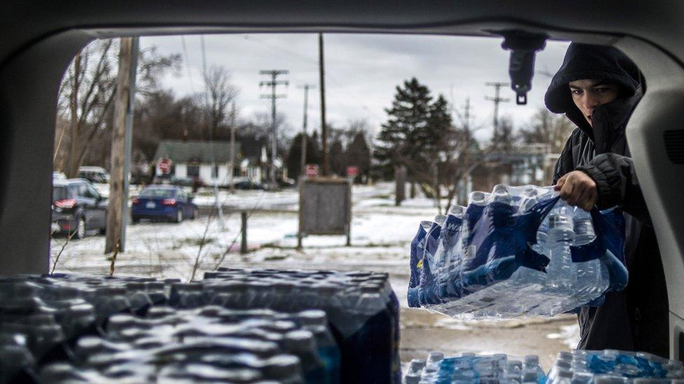 Flint, Michigan, resident Randy Huyck Jr., 17, throws a case of bottled water into the back of a volunteer's car as Detroit-area volunteers drop off more than 500 cases of bottled water in Flint on Saturday, Jan. 16, 2016.