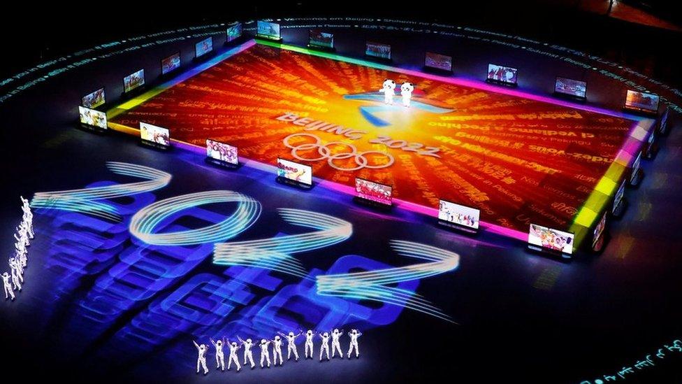 Figures gather around a giant projected logo of the Beijing 2022 Olympics