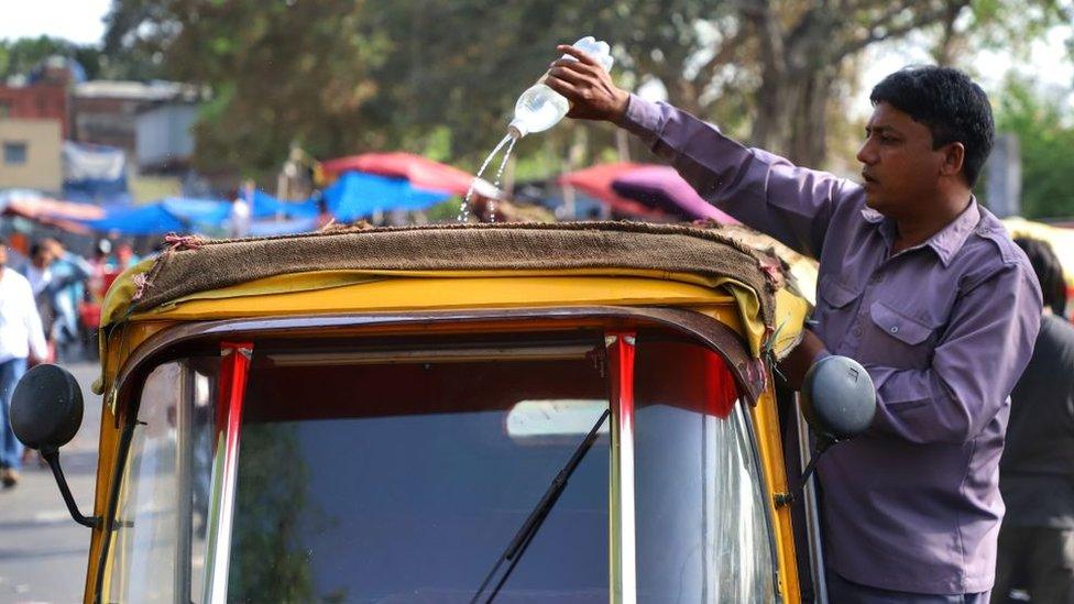 A tuktuk driver pours water on the roof of his vehicle on a hot summer day in New Delhi, India, on 14 April 2019.