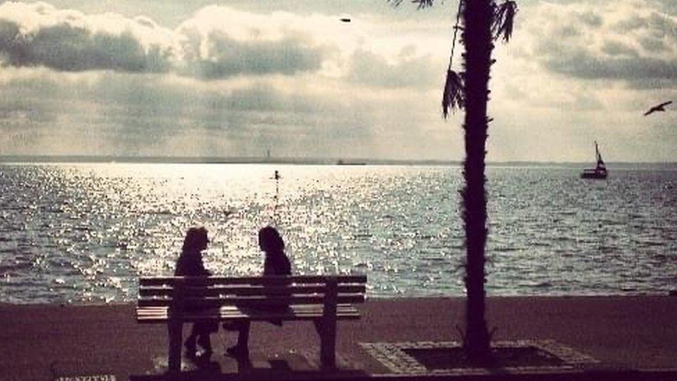 Janet sitting on a bench by the sea