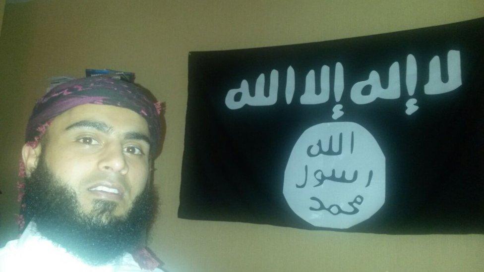 Ayman Shaukat by a flag linked to Islamic State fighters