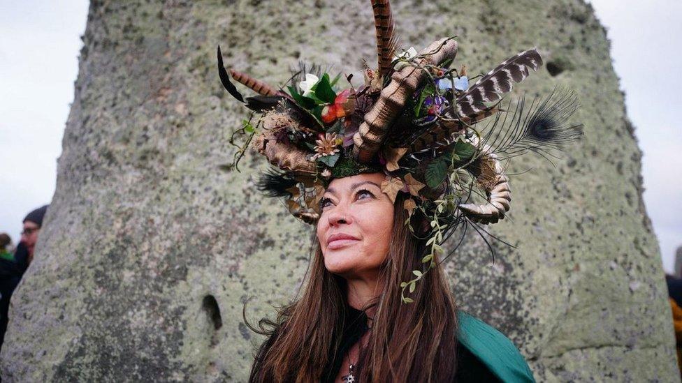 Woman in headdress looking up, in front of a stone at Stonehenge