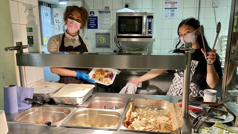 Two women behind a food serving buffet