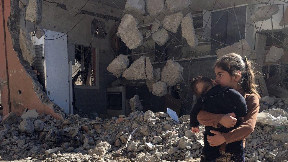 A young girl holds a child in front of a ruined house in Cizre, Turkey, Wednesday, March 2, 2016.