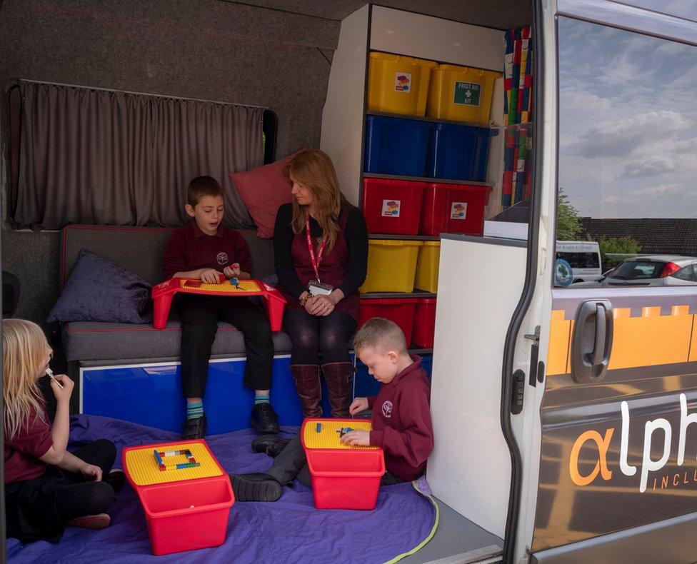 Three children sat with trays full of Lego listen to their mentor Caryn