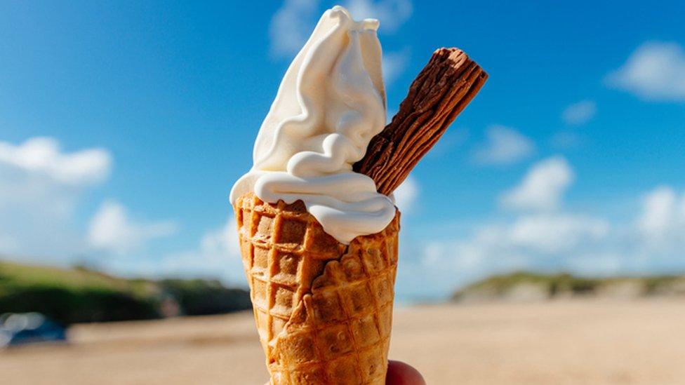 An ice cream with a chocolate flake being held against a bright blue sky