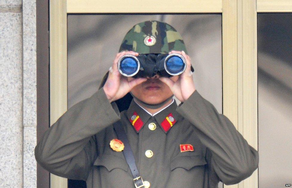 A North Korean soldier using binoculars watches from his patrol quarters