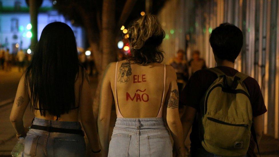 Women, one with the words "not him" painted on her back, demonstrate in Rio de Janeiro