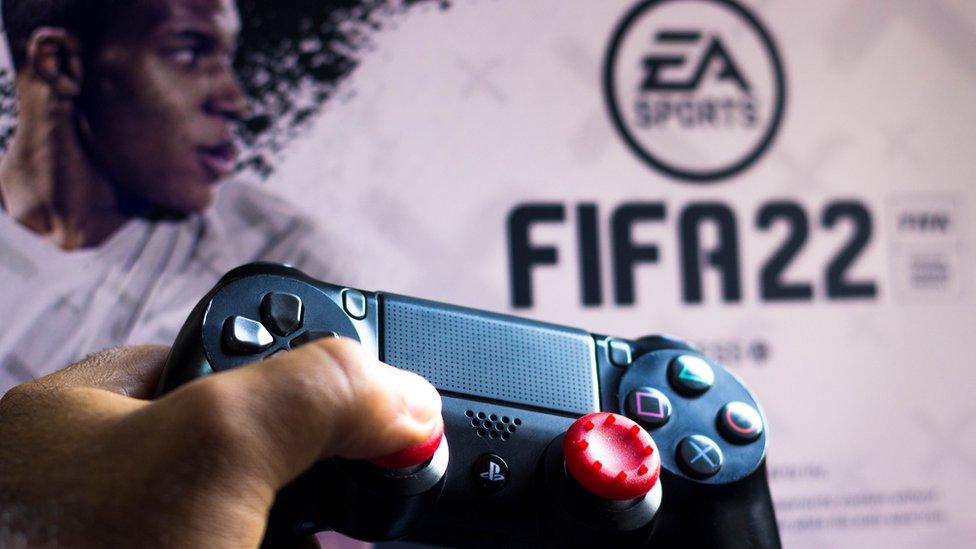 This stock photo shows a Playstation controller being held in front of a Fifa 22 logo