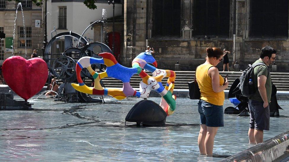 Two persons soak their feet in the water of in the Stravinsky fountain in Paris