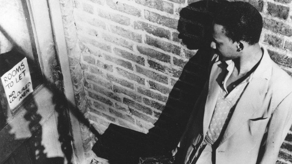 A Caribbean migrant reading a sign on a boarding house door