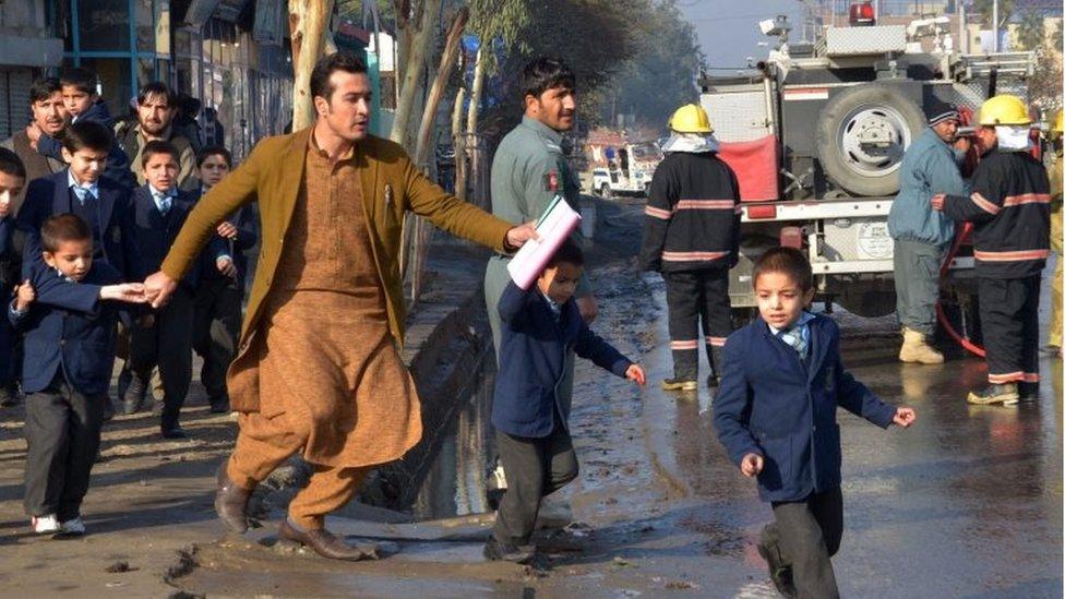 An Afghan teacher, in brown, helps school children run from the site of clashes near the Pakistan consulate in Jalalabad, capital of Nangarhar province, Afghanistan, Wednesday, Jan. 13, 2016.