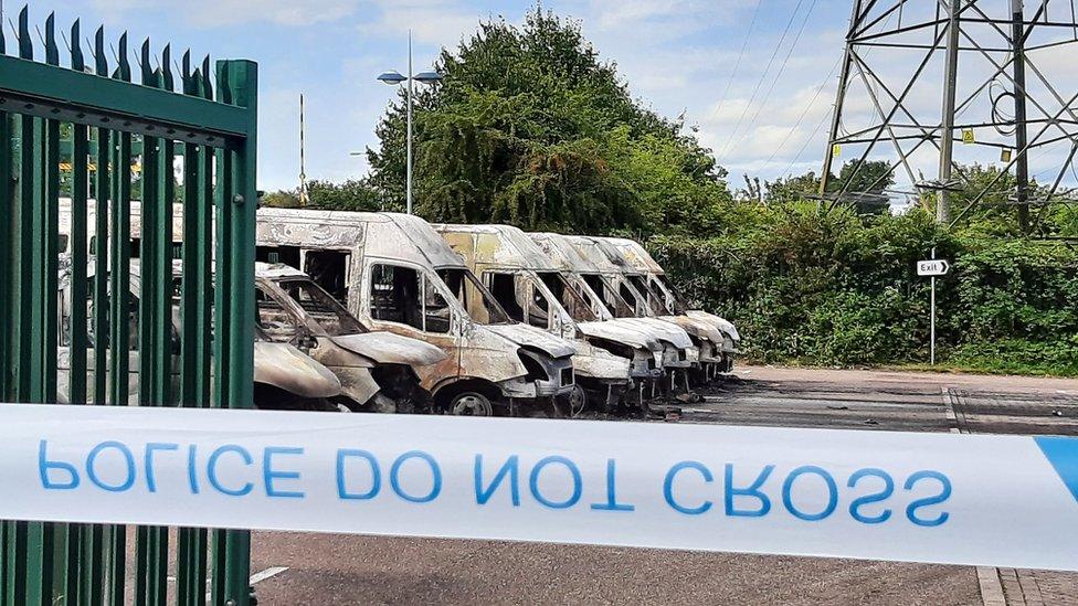 Fire-damaged minibuses with police do not cross tape in foreground