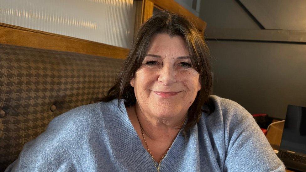 Kim Knight, a white woman with brown hair and wearing a light blue top smiles into the camera.