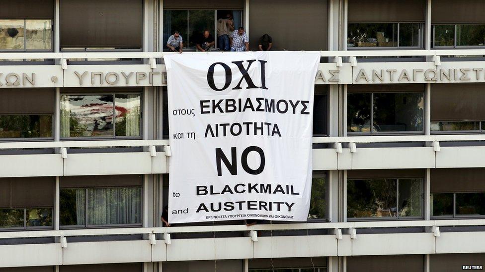 Employees stand by a banner unfolded from a balcony of the Finance Ministry in Athens