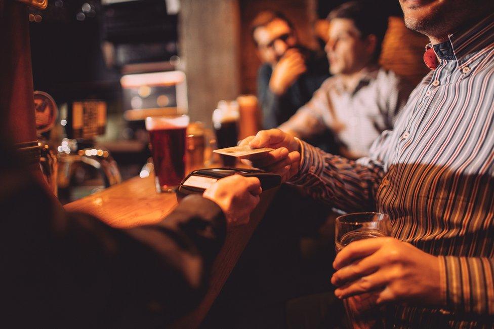 Man paying for drinks in pub with contactless card