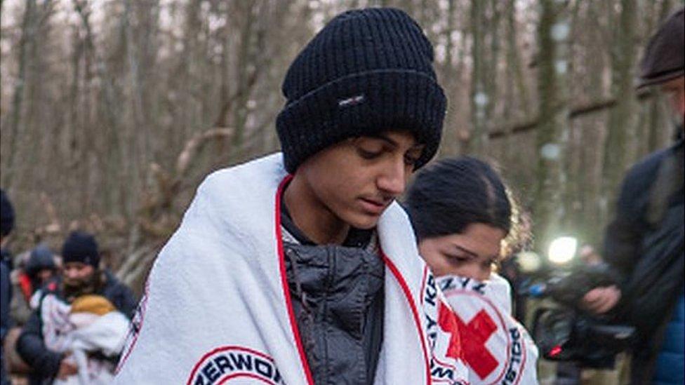 A migrant family warm themselves with red cross blankets in a Polish forest