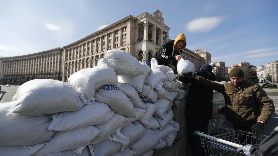 A group of men is seen unloading sand bags from a shopping trolley to make a barrier in downtown Kyiv