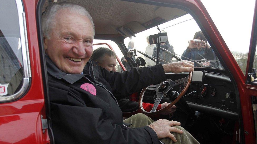 Paddy Hopkirk sitting in a red Mini Cooper, a replica of his Monte Carlo rally-winning car