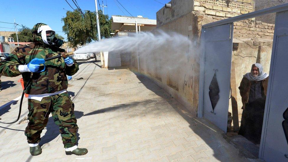 An Iraqi man looks out of a doorway as a civil defence worker disinfects an area of Najaf where Covid-19 cases have been detected (3 February 2020)