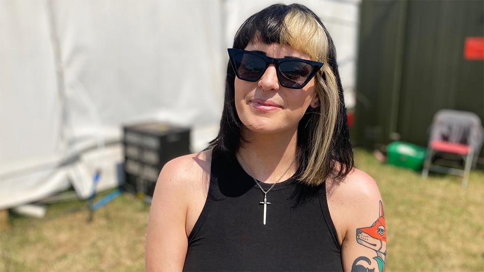 Creeper keyboardist and vocalist Hannah Greenwood smiling for the camera. She is wearing sunglasses and has a black vest on with a tattoo of a fox on her left arm