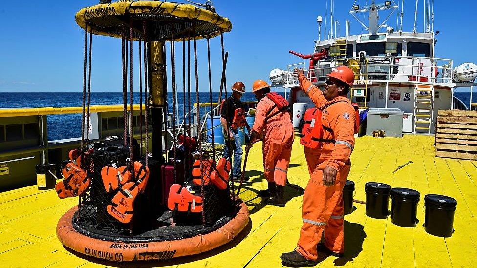 Three scientists in orange work gear on a large boat.