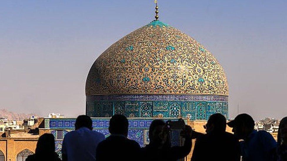 Silhouettes of tourists looking at Sheikh Lutfollah Mosque while standing on the eastern side of Naqsh-e Jahan Square