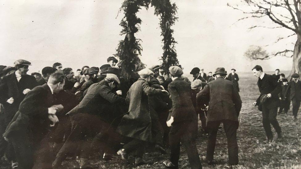 Men wearing suits and caps surrounding the goalposts known as hales in the 1920s