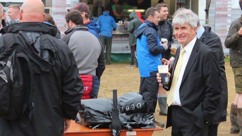 Aelod o gor yn ei siwt yn cael peint ar y Maes // A choir member enjoys a pint on the Eisteddfod field