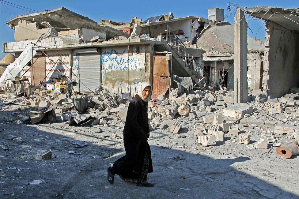 A Syrian woman walks past buildings destroyed in a reported government air strike in the town of Maasaran in Idlib province, 17 December 2019