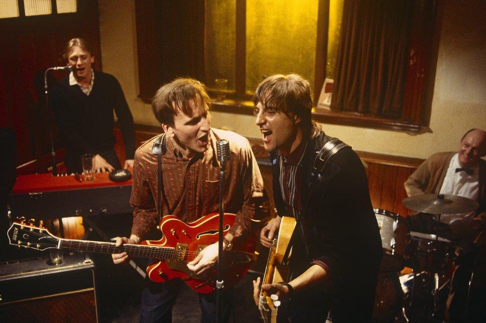 Christopher Eccleston (left) and Mark Strong (right) playing guitars in episode one