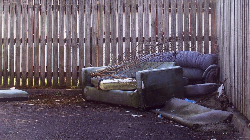 Sofas abandoned against a fence