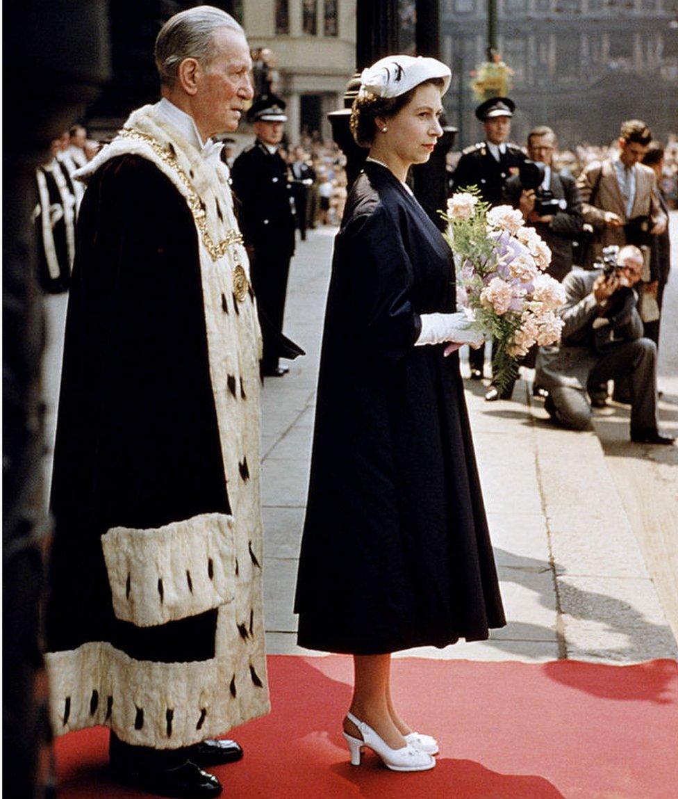 Queen Elizabeth II standing on a red carpet with a posy of flowers