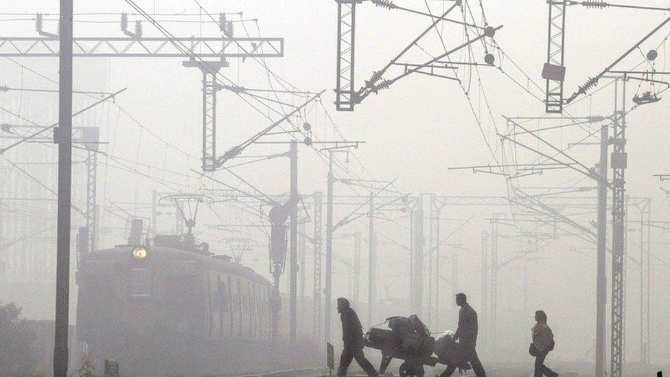 A porter carries the luggage of a passenger as a local train arrives amidst morning fog at Nizamuddin railway station in New Delhi, India, Friday, Jan. 2, 2004.