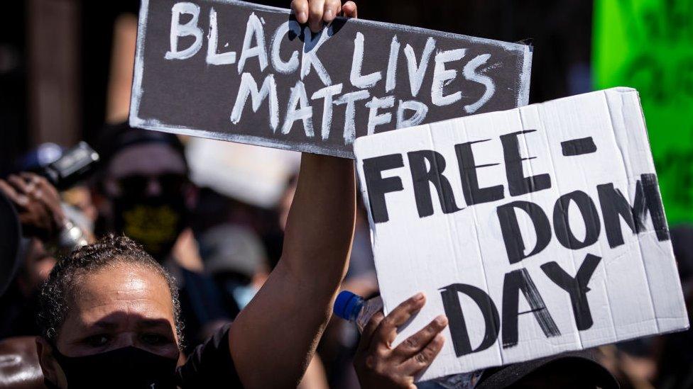 Protesters hold homemade signs that reads, "Free-Dom Day" and "Black Lives Matter" as they perform a peaceful protest walk