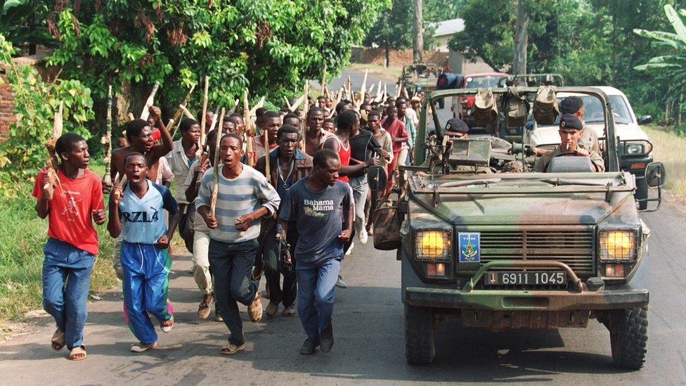 French soldiers on patrol pass ethnic Hutu troops from the Rwandan government forces 27 June 1994, near Gisenyie, about 10kms from the border with Zaire.