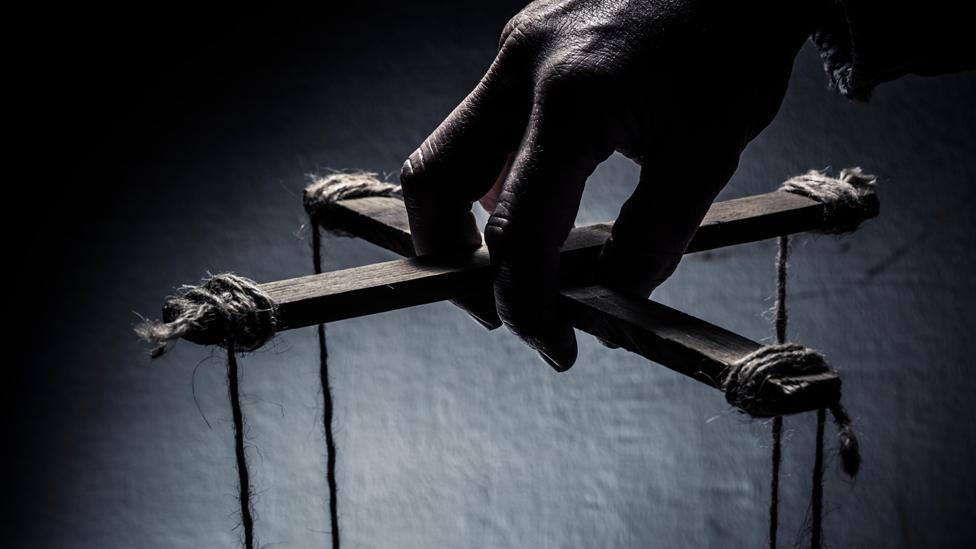 Dark hand of puppet master controls strings (stock photo)